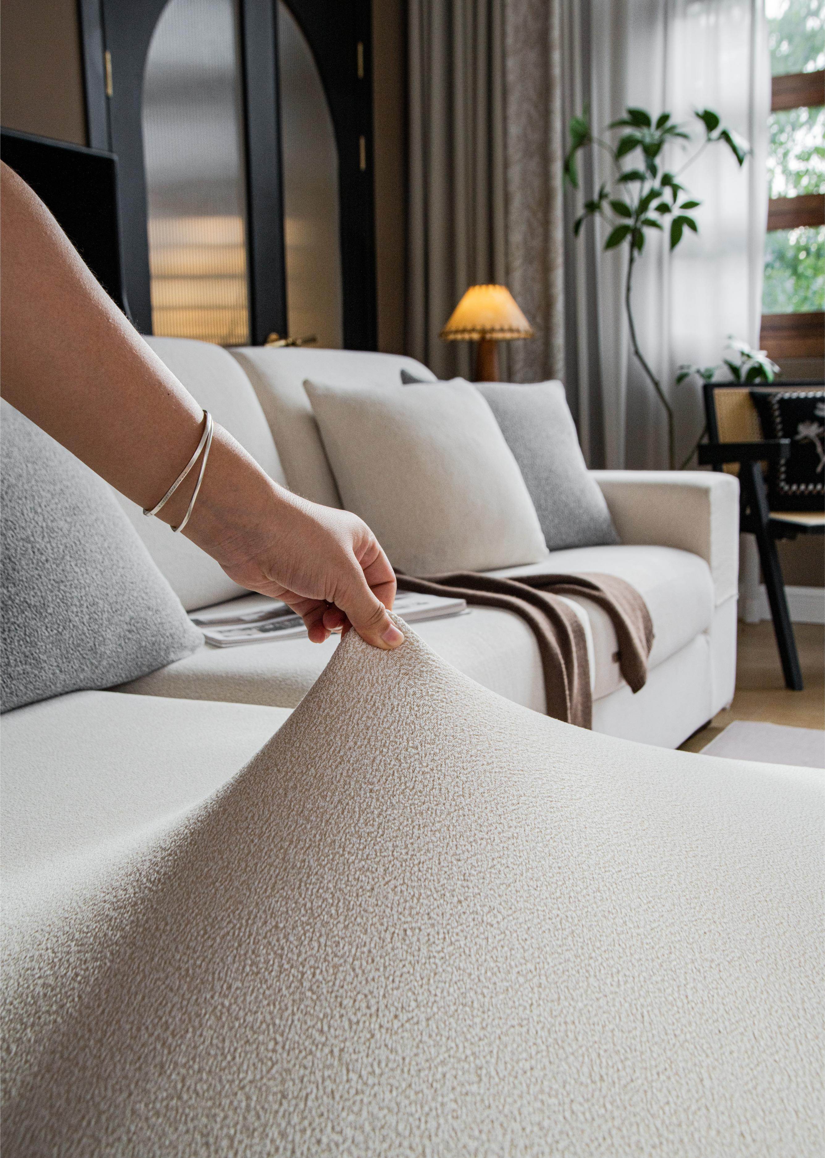 Close-up of the Cozee Cozura Sofa Cover fabric pinched between fingers, highlighting thick chenille texture and skin-friendly softness.