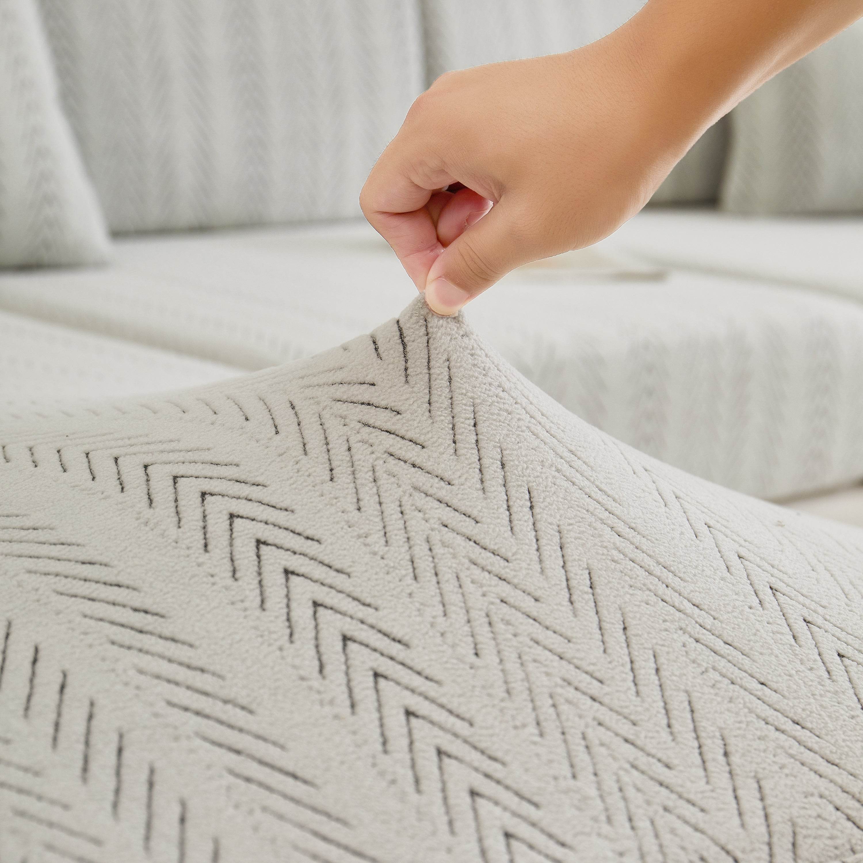 Close-up of the Cozee Herringbone Sofa Cover fabric being pinched between fingers, showing thick soft herringbone texture and durable quality.