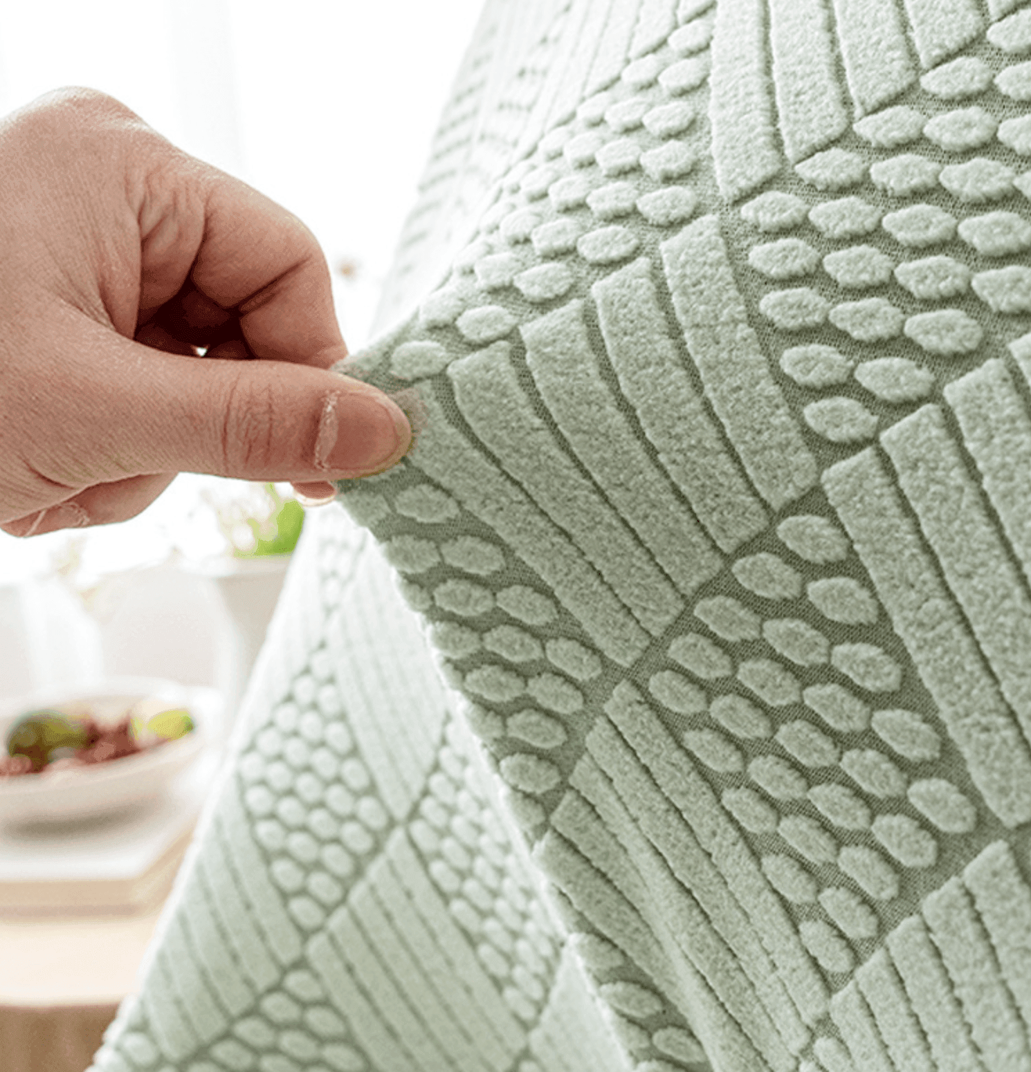 Close-up of a hand pulling textured mint green jacquard fabric, highlighting the stretchability, intricate weave, and soft flexibility of the Cozee Curved Chair Cover