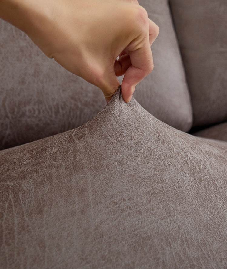 Close-up of hand pinching the Cozee Lux slipcover fabric to show its elasticity, soft texture, and high-stretch performance