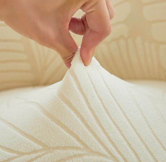 Close-up of hand pinching ultra-soft velvet fabric on the SoftWeave chair cover, showing its flexible stretch and plush texture with embossed leaf detail