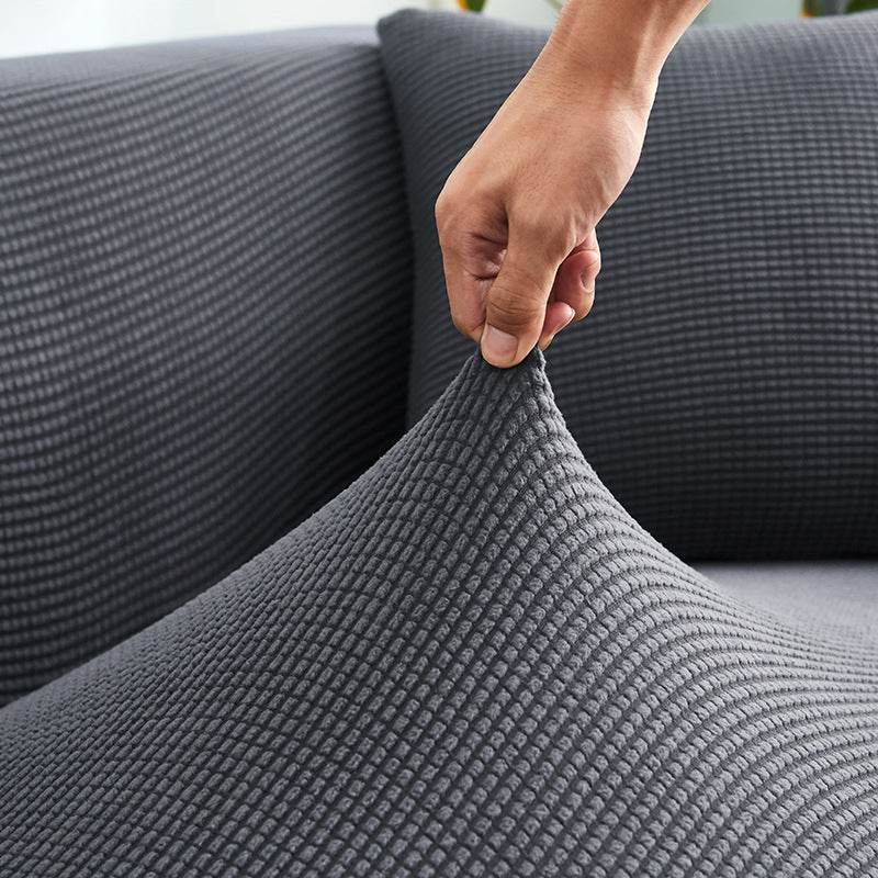 Close-up of a hand pinching the plush fabric of the Cozee Timeless Slipcover, highlighting its ultra-soft texture and high elasticity for a snug, secure fit