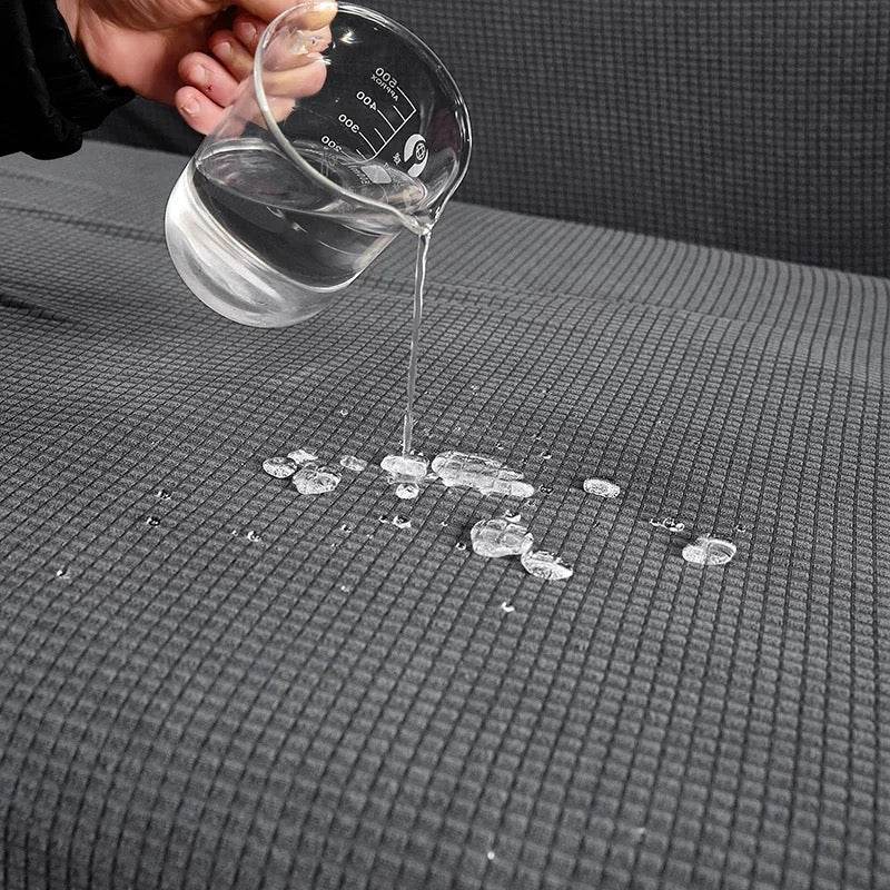 Water being poured from a clear container onto the textured surface of the Cozee Timeless Slipcover, demonstrating its water-resistant fabric that guards against spills and daily messes
