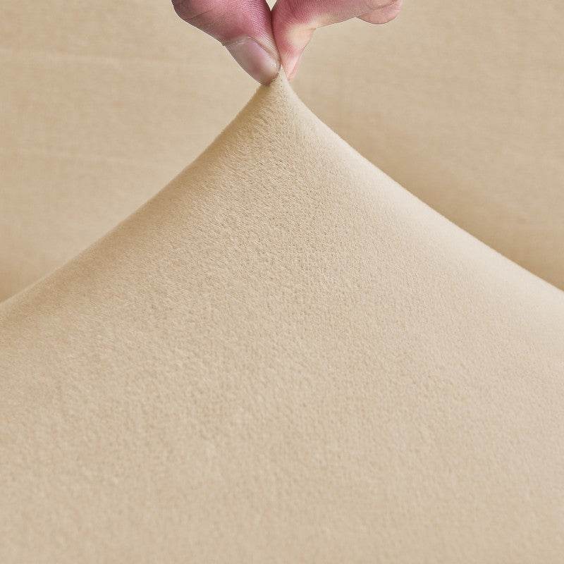 Close-up of plush sofa cover fabric with a hand lifting the corner, highlighting the soft texture, stretchability, and easy handling of the Cozee Ultra Soft Plush Slipcover