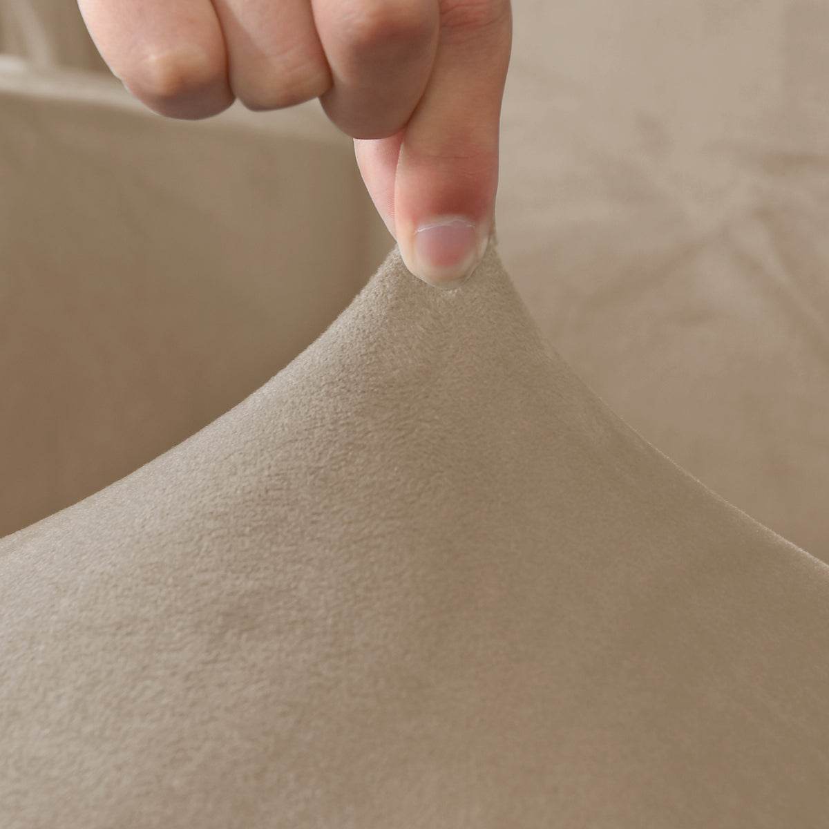 Close-up of a hand holding textured beige velvet slipcover fabric, showcasing its soft feel, stretchability, and premium quality